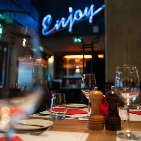 Ein gedeckter Tisch mit Blick auf den Eingang der Küche über dem groß und leuchtend "Enjoy" steht.